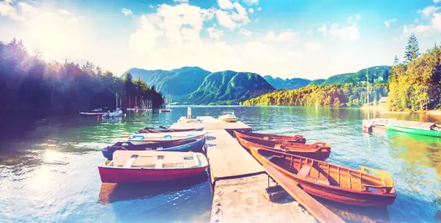Un lago sereno incastonato tra montagne verdeggianti, con un villaggio pittoresco e barche colorate lungo le rive