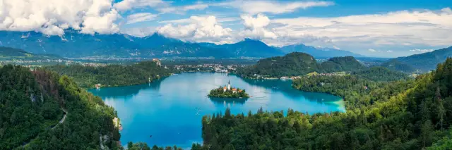 Paesaggio del lago di Bled con l'iconica chiesa su un'isola e il castello arroccato su una scogliera che domina l'acqua