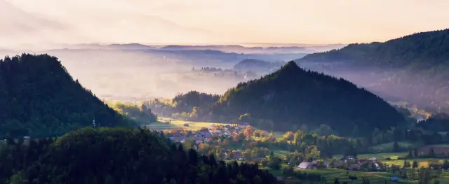 Un paesaggio sereno di dolci colline e foreste verdeggianti, con un fiume cristallino che serpeggia nella valle, che mostra la bellezza del turismo sostenibile in Slovenia.